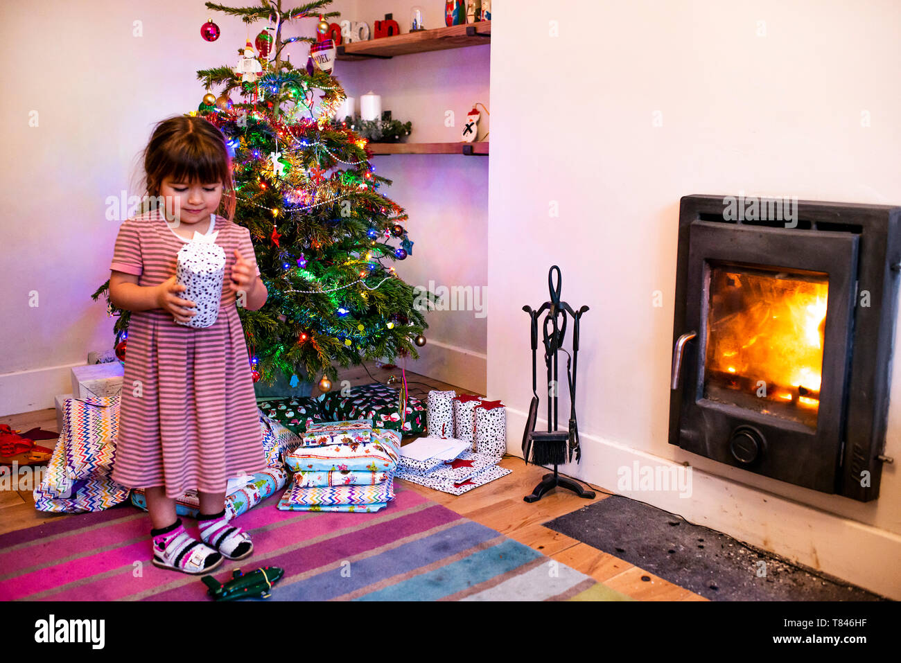Girl standing next to living room christmas tree looking at christmas present Stock Photo