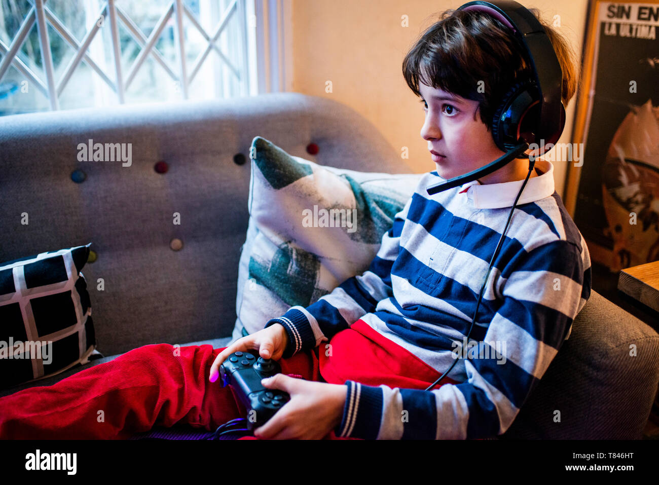 Boy sitting on sofa wearing headset and  using game controller Stock Photo