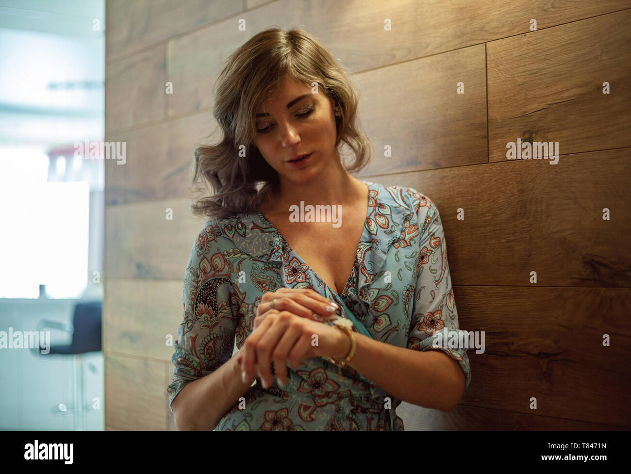 Woman checking time, leaning against wooden wall Stock Photo