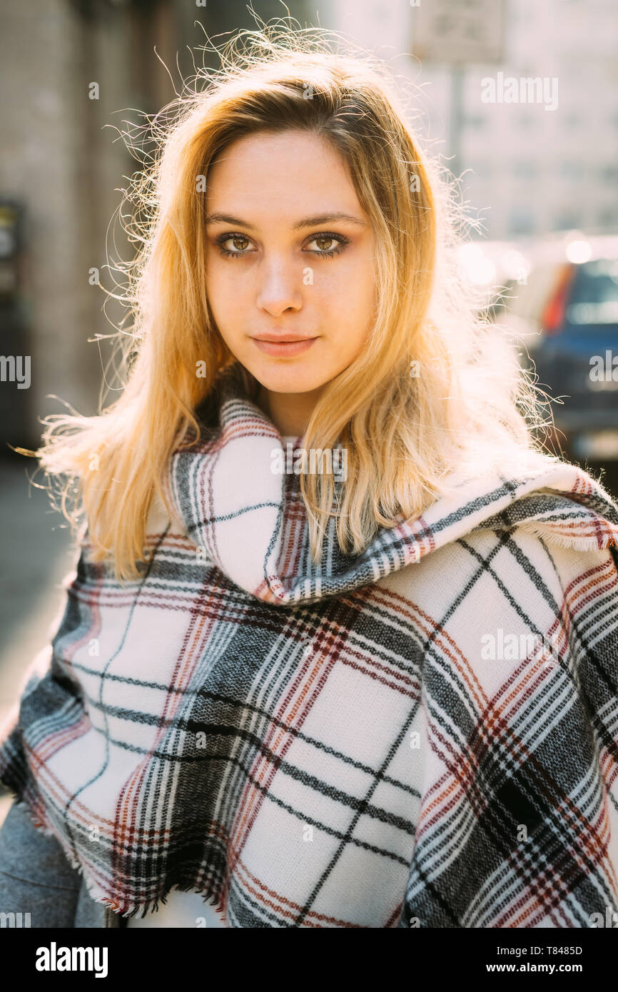 Young woman with long blond hair wrapped in shawl on city street Stock Photo