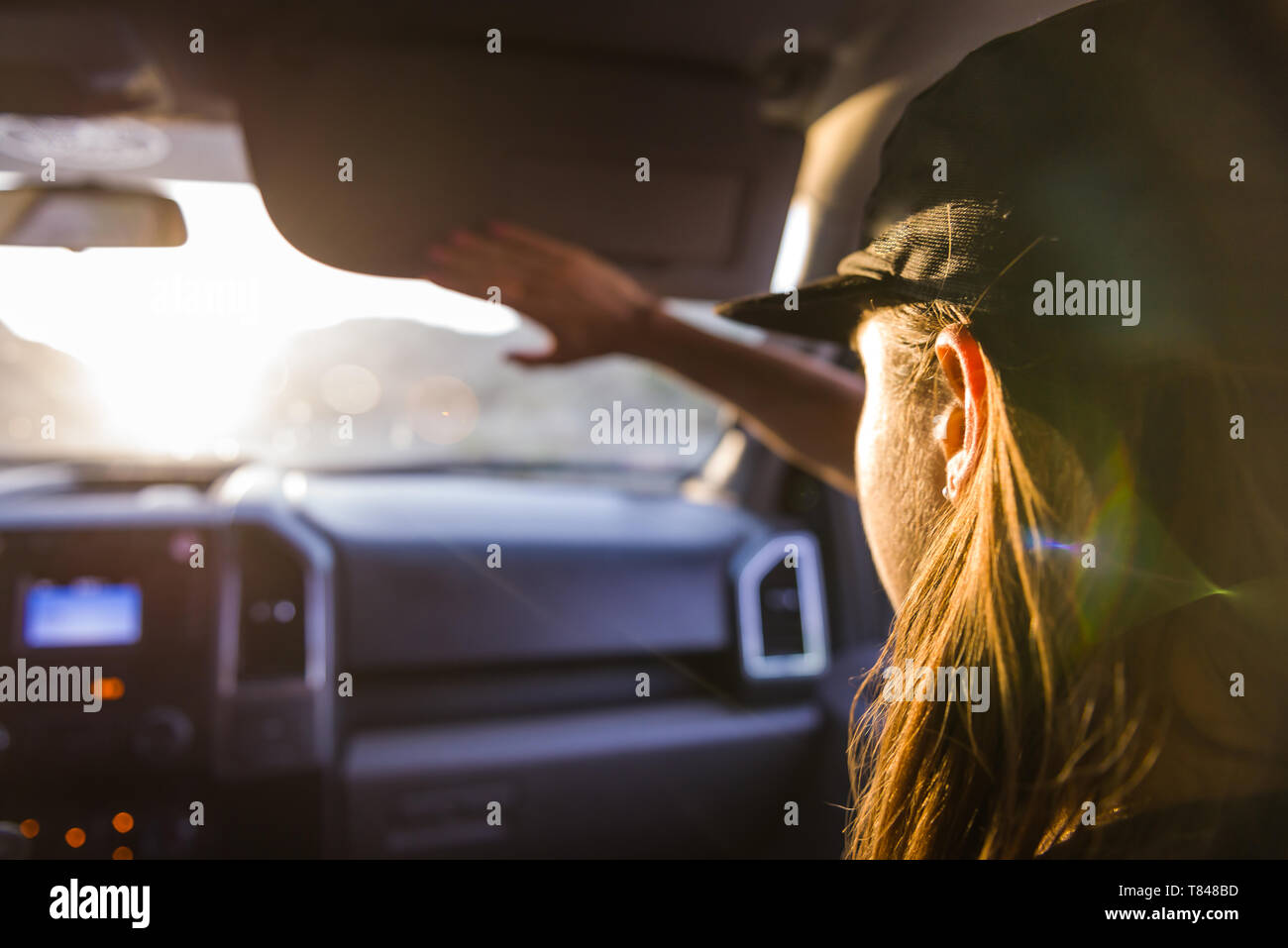 Woman passenger in front seat of car shielding eyes from sunlight, over shoulder view Stock Photo