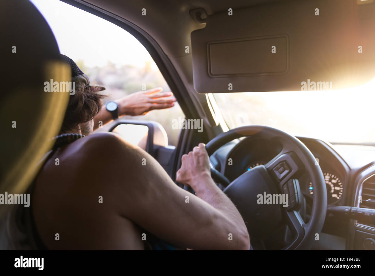 Man driving car shielding eyes from sunlight, over shoulder view Stock Photo