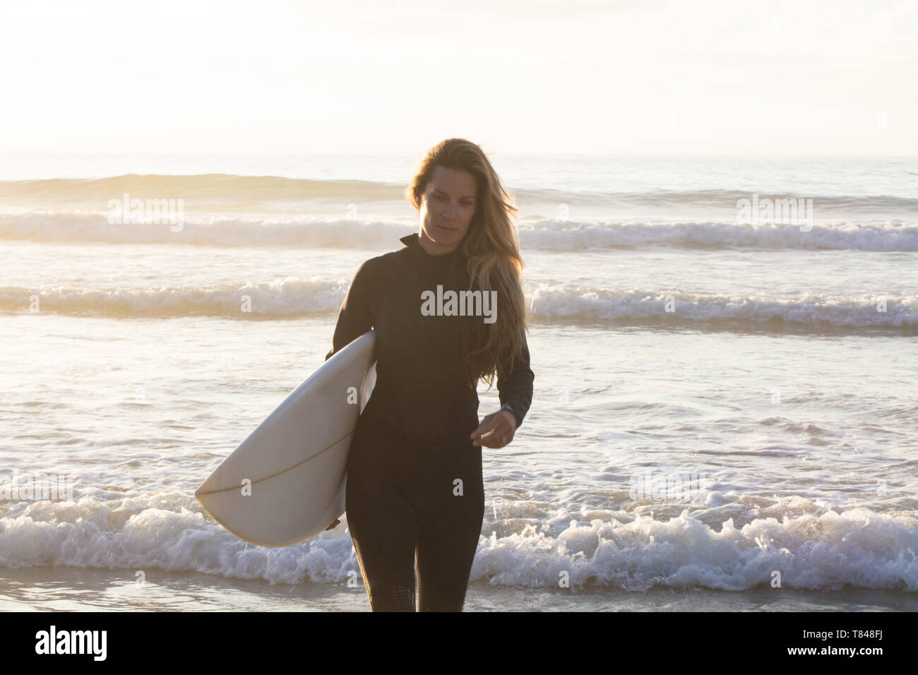 Female surfer carrying surfboard from sea, Cape Town, Western Cape