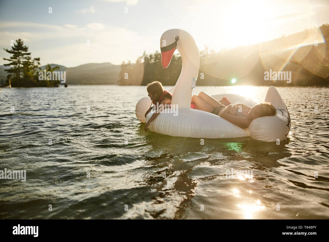 Girls playing on inflatable swan in lake Stock Photo