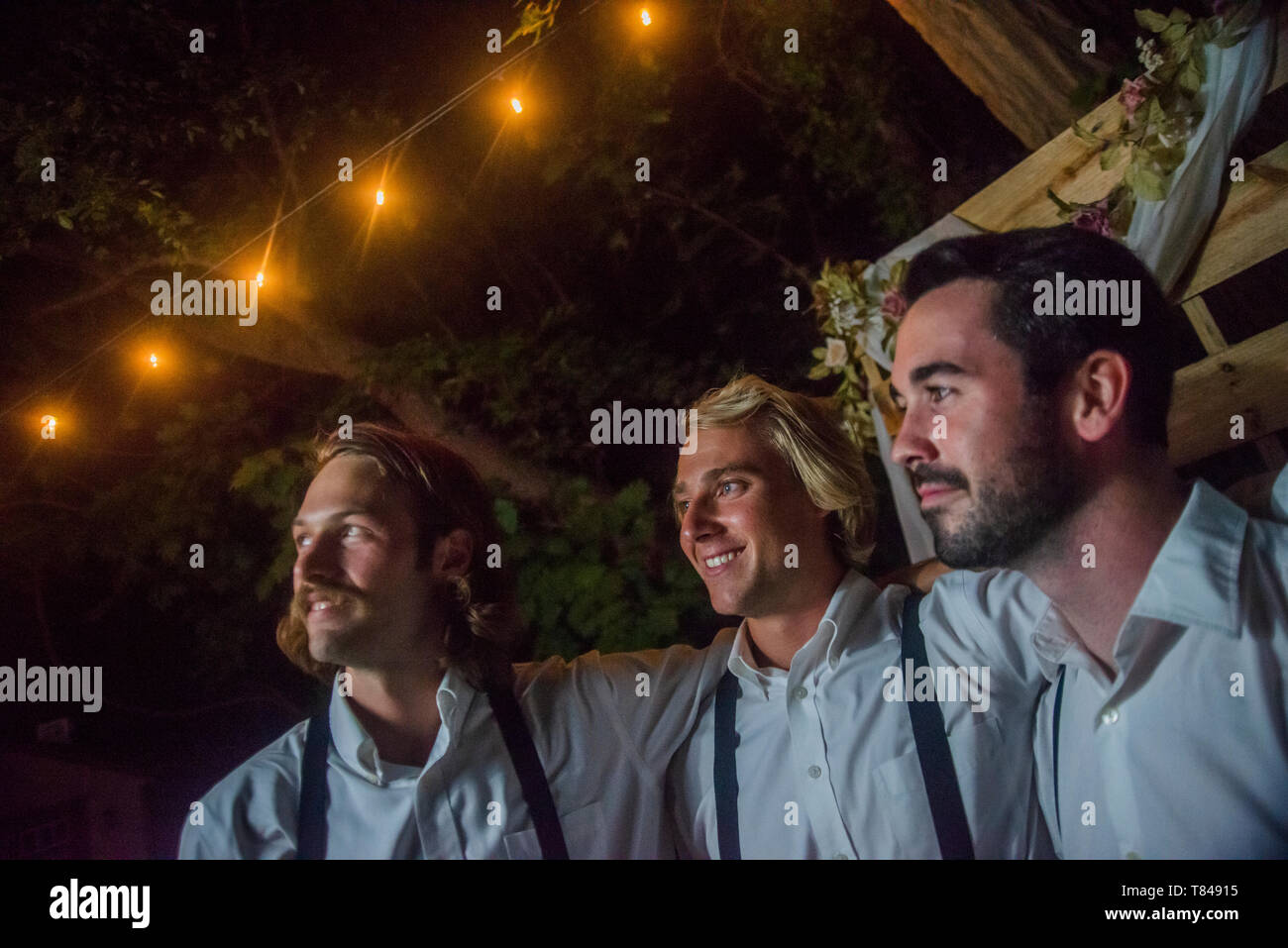 Three young men with arms around each other at outdoor wedding ...