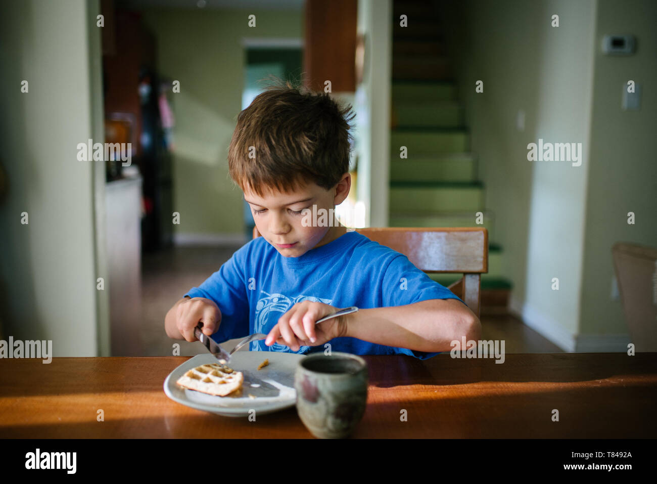 Boy eating waffle breakfast at kitchen table Stock Photo