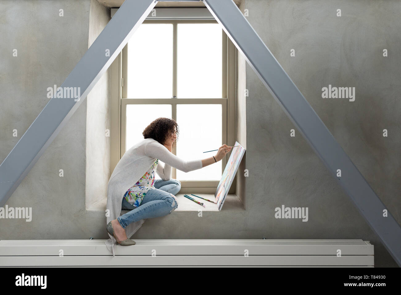 Young female painter painting canvas on studio windowsill Stock Photo