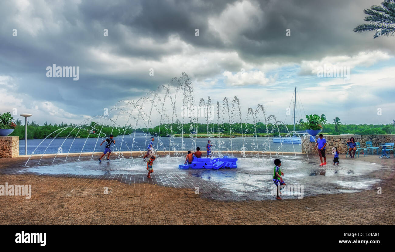 Grand Cayman, Cayman Islands, Aug 2018, kids playing by a water fountain on a plaza of Camana Bay a modern waterfront town in the Caribbean Stock Photo