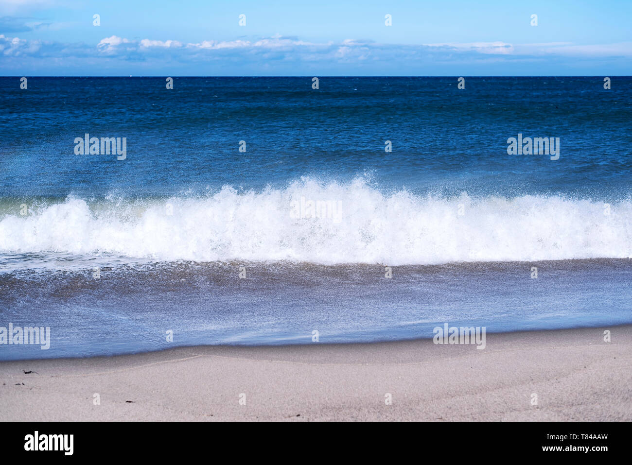 Waves from the Atlantic Ocean crashing onto the beaches of the Cape Cod National Seashore in Truro Massachusetts on a sunny blue sky day. Stock Photo