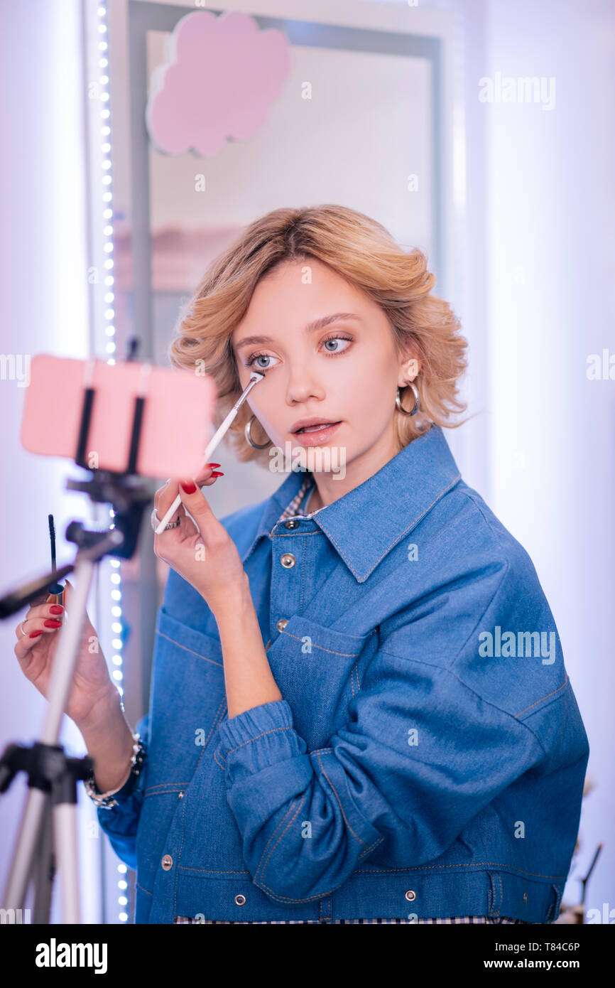 Blogger wearing denim jacket doing makeup and filming it Stock Photo