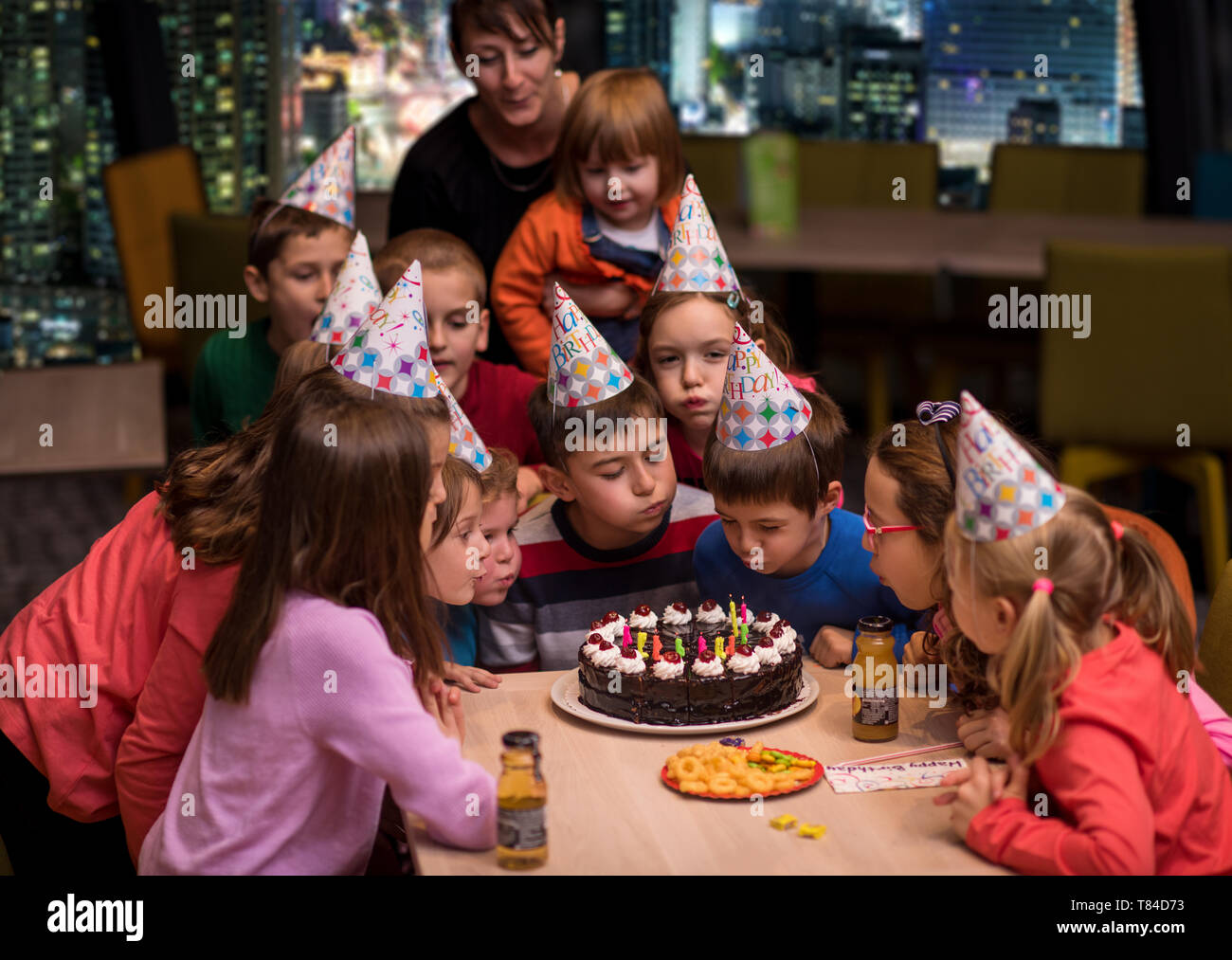 young happy boy and group of his friends having birthday party with a night city through the windows in the background Stock Photo