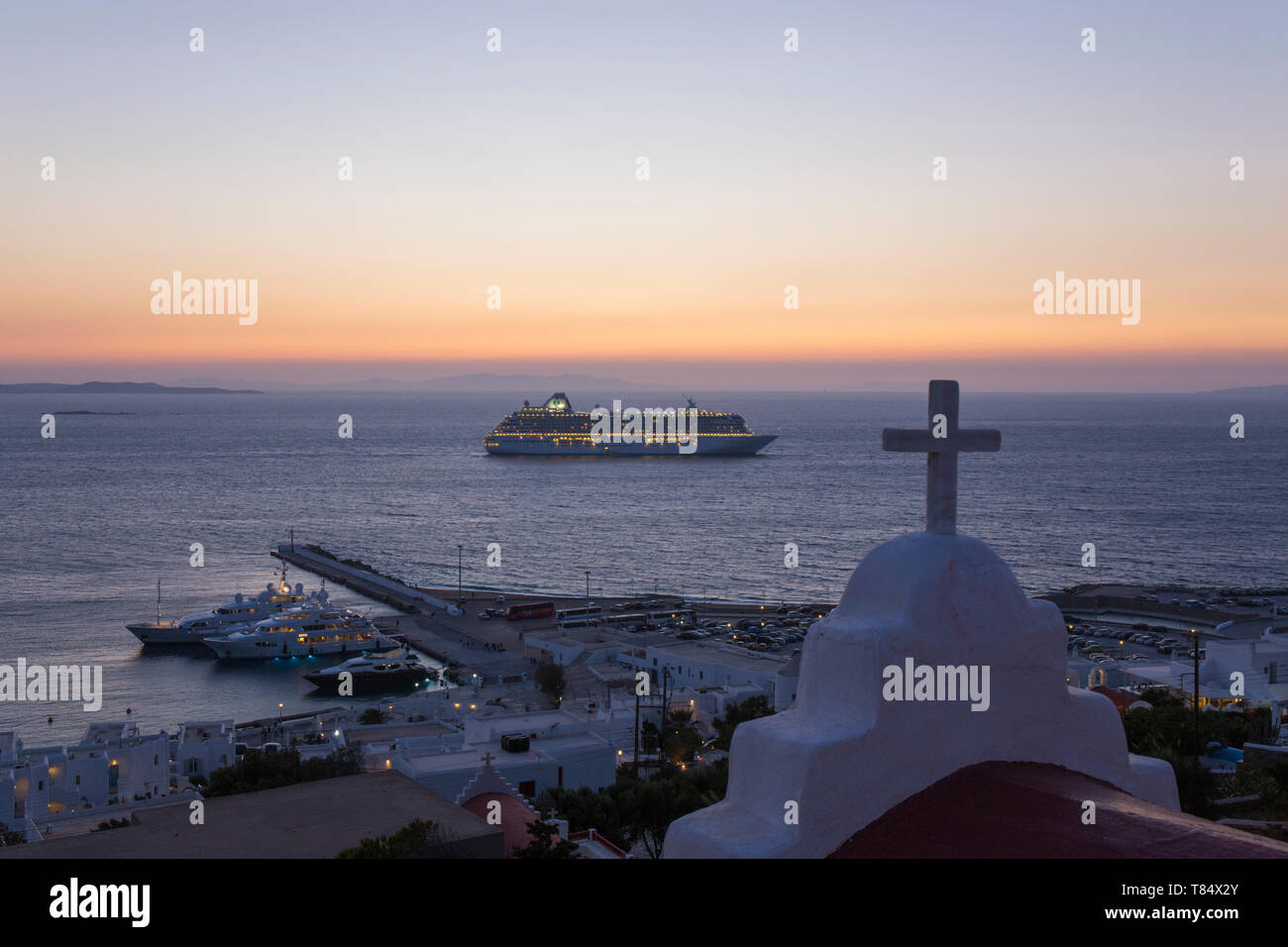 Mykonos Town, Mykonos, South Aegean, Greece. View across the Aegean Sea from hillside, dusk, illuminated cruise ship anchored offshore. Stock Photo