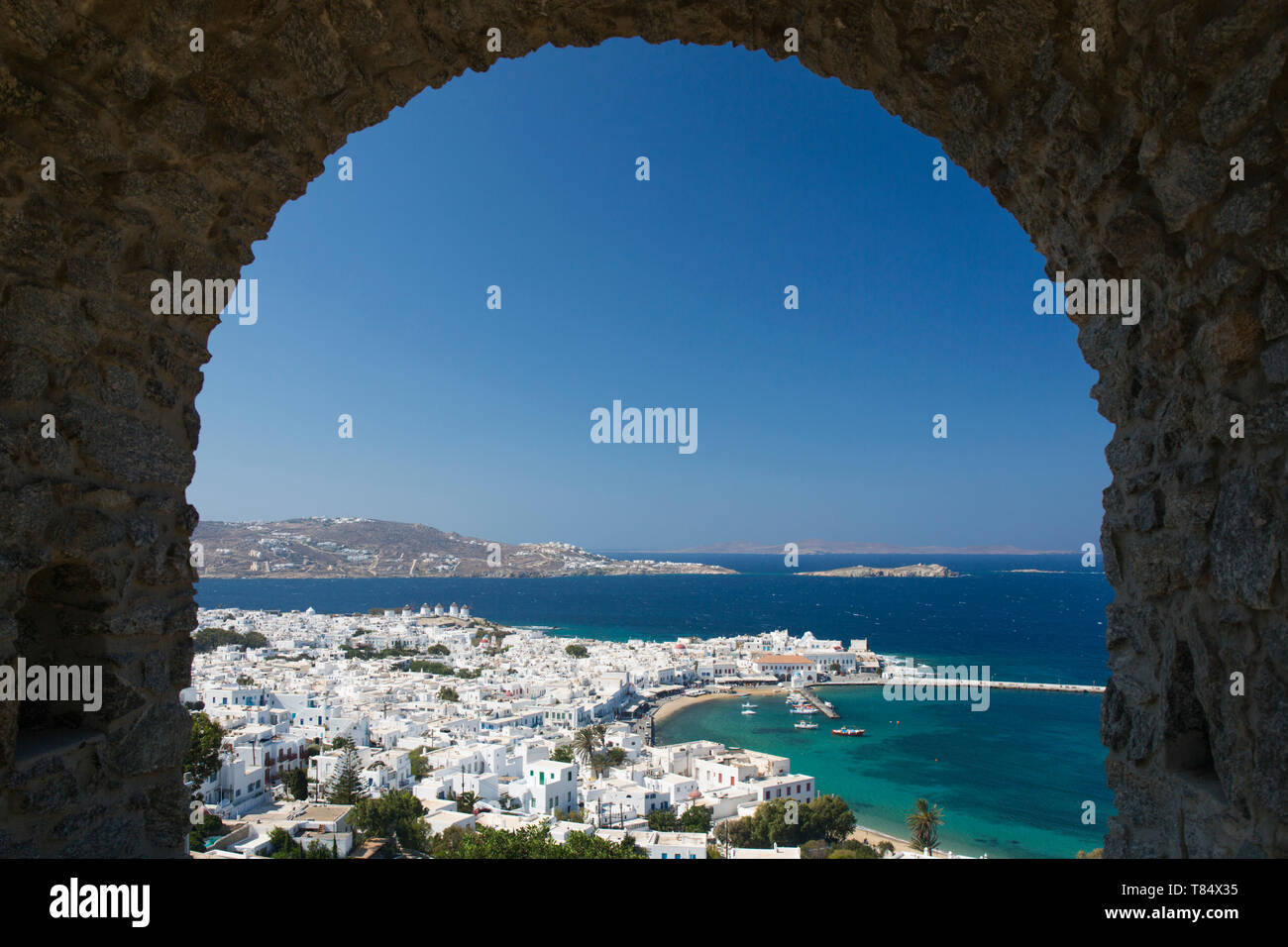 Mykonos Town, Mykonos, South Aegean, Greece. View over the town and harbour through stone archway in the castle ramparts. Stock Photo