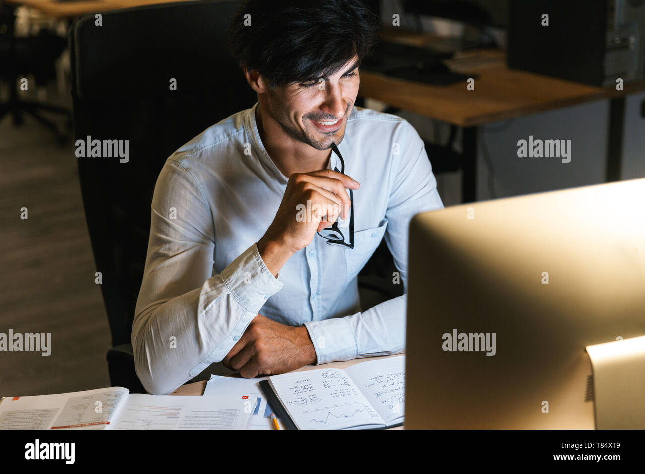 Smiling young man working at the office late at night, using computer Stock Photo