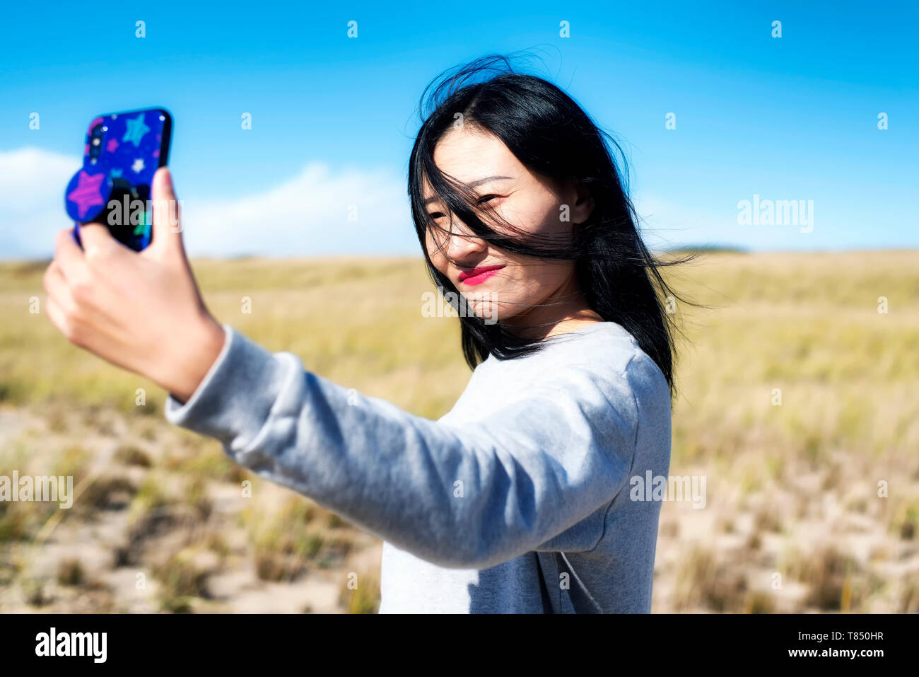 A chinese womantaking a selfie on a sunny windy day on the cape cod national seashore in Truro Massachusetts. Stock Photo