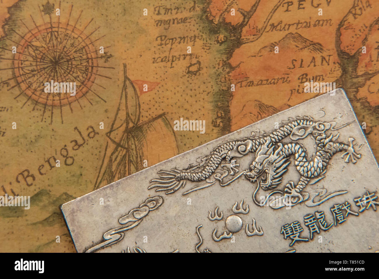 Antique silver plate with fighting dragons On Ancient oriental-style World Map. Symbol of Eternal struggle of Good and Evil. Closeup. Indoors. Stock Photo