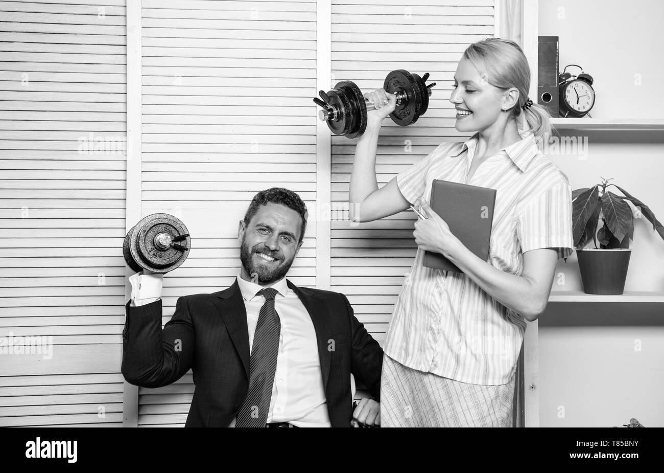 Man and woman raise heavy dumbbells. Strong powerful business strategy. Good job concept. Boss businessman and office manager raise hand with dumbbells. Strong business team. Healthy habits in office. Stock Photo