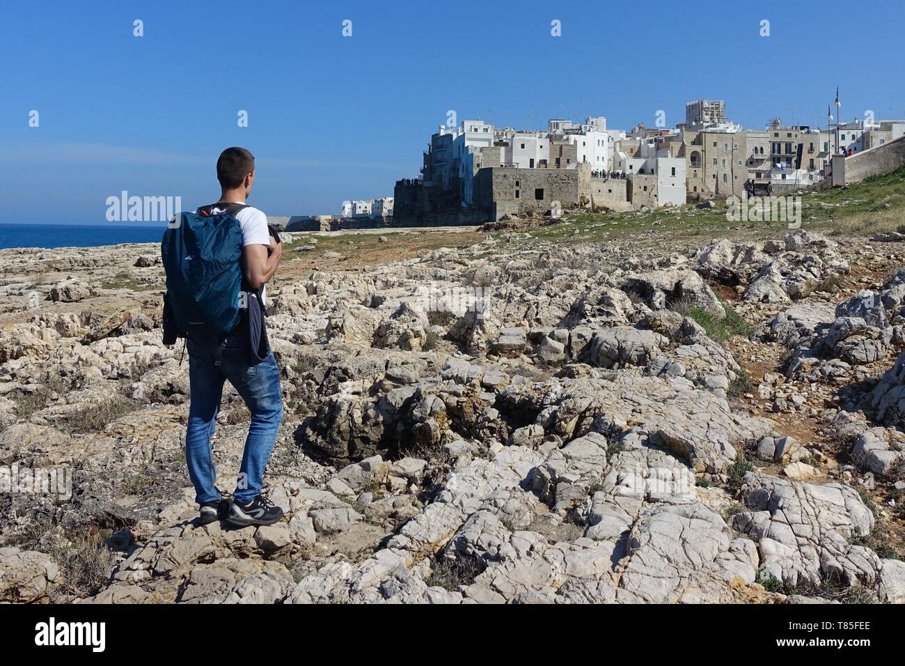 Traveller arriving to medieval town through rocks, Polignano a Mare near Bari, Italy wallpaper Stock Photo