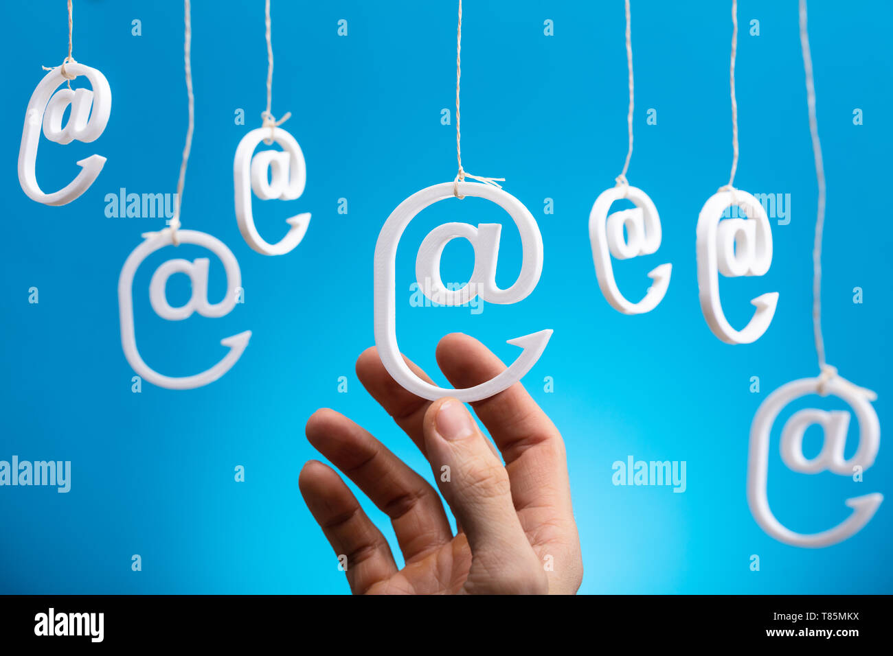 Human's Hand Holding Hanging Email Icons Against Blue Background Stock Photo