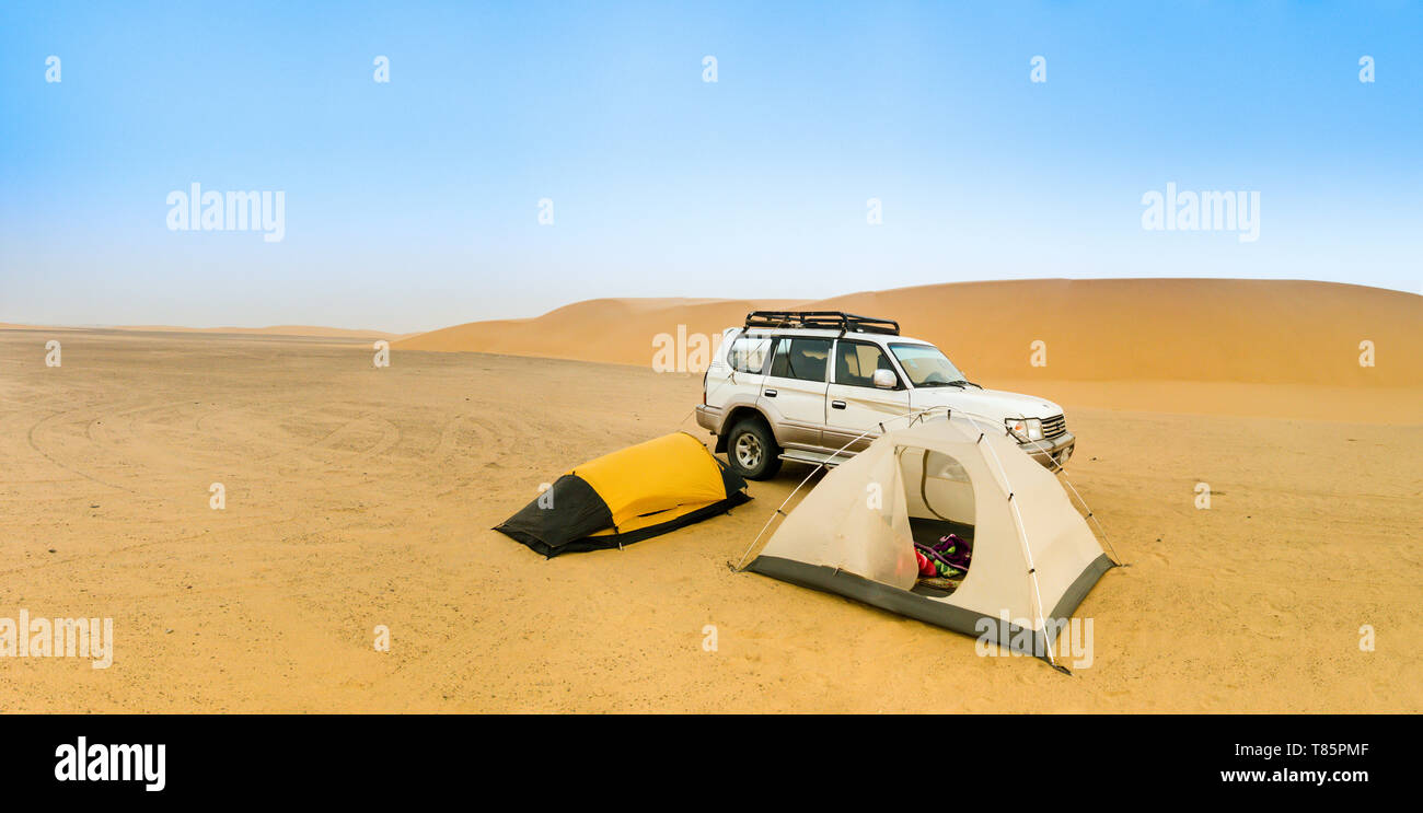 Camping in the Sudanese desert with two small tents, an off-road vehicle and a sand dune in the background, panorama. Stock Photo