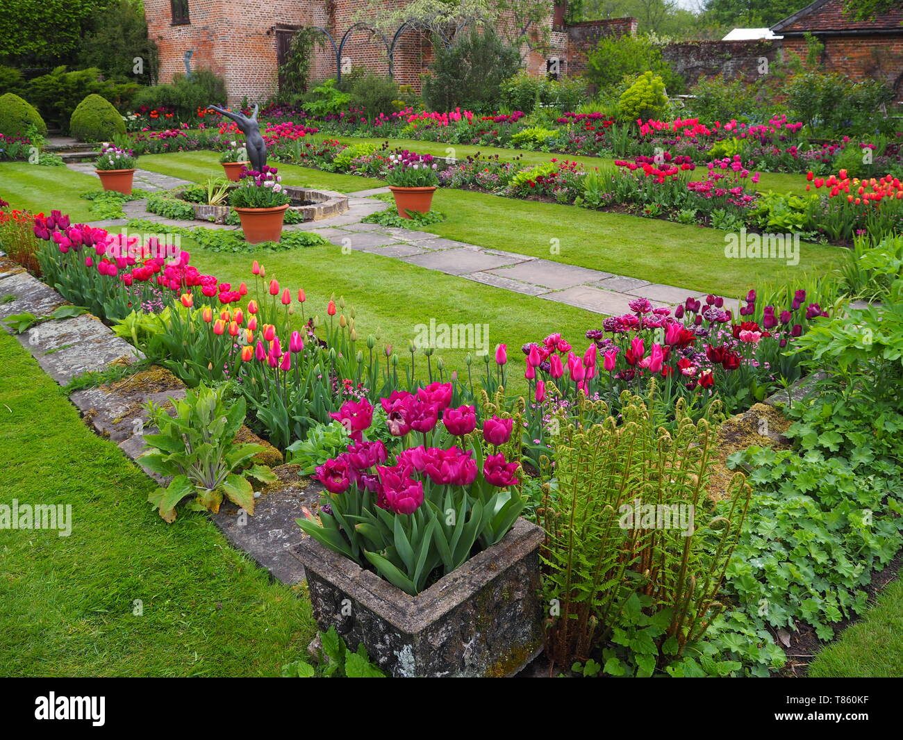 Chenies Manor Sunken Garden with Pavilion and pond in early May showing colourful tulips, sculpture and fresh green foliage beautifully landscaped. Stock Photo