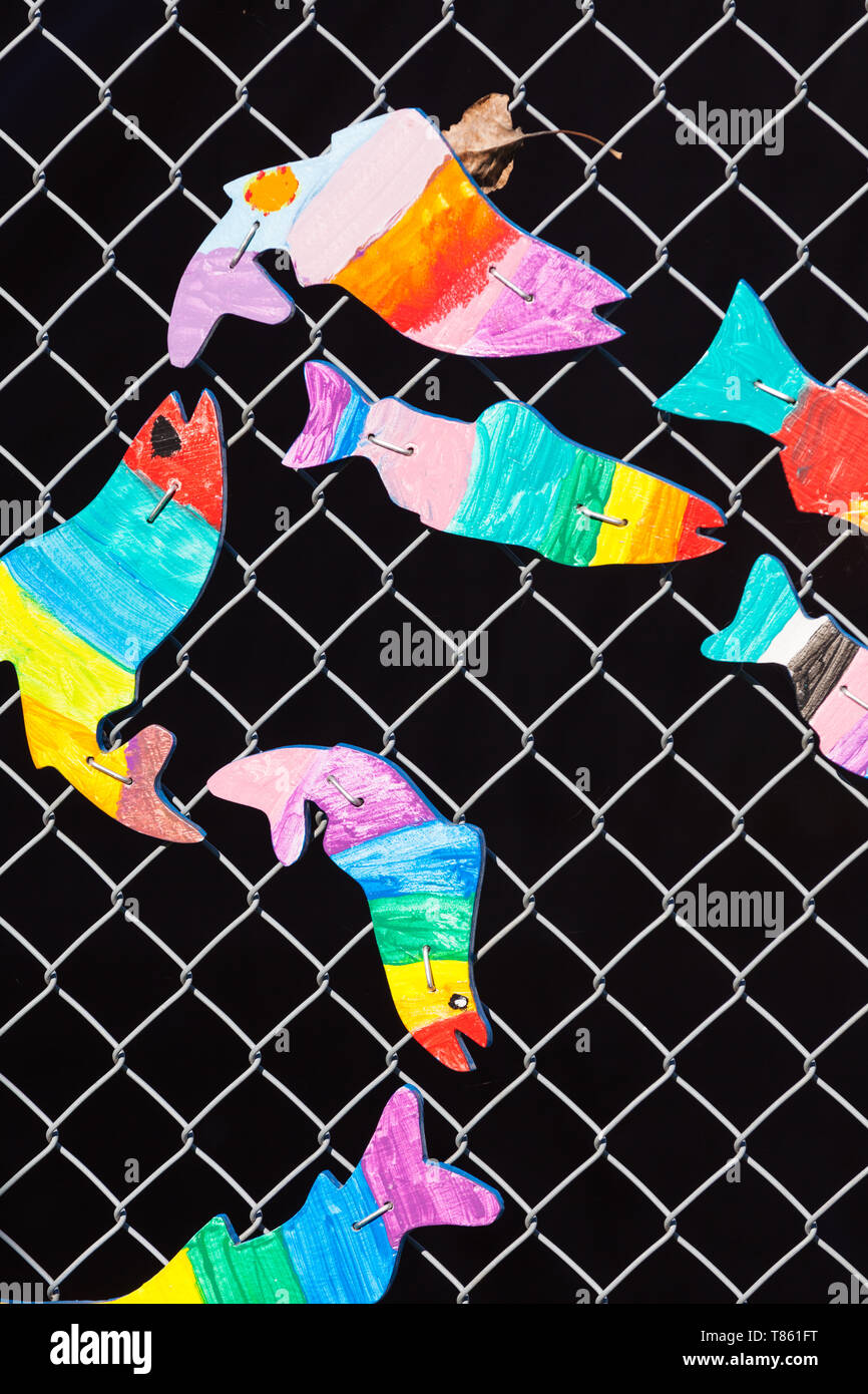 Fish profiles painted by children and mounted to a wire mesh fence Stock Photo