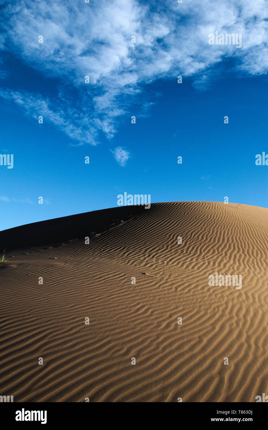 Large sand dune beneath a blue sky with clouds, in the desert of ...