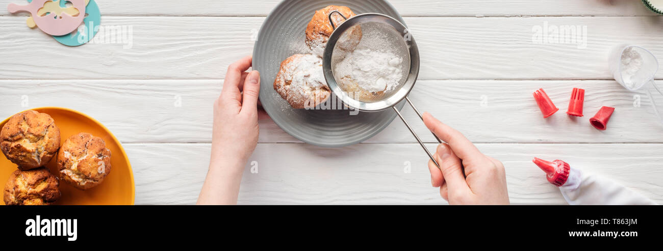 panoramic shot of woman decorating cupcakes with powdered sugar on white table Stock Photo