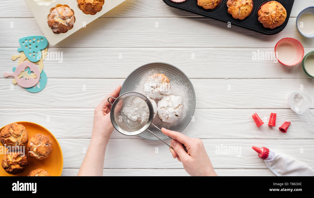 partial view of woman decorating cupcakes with powdered sugar on table with baking tools Stock Photo