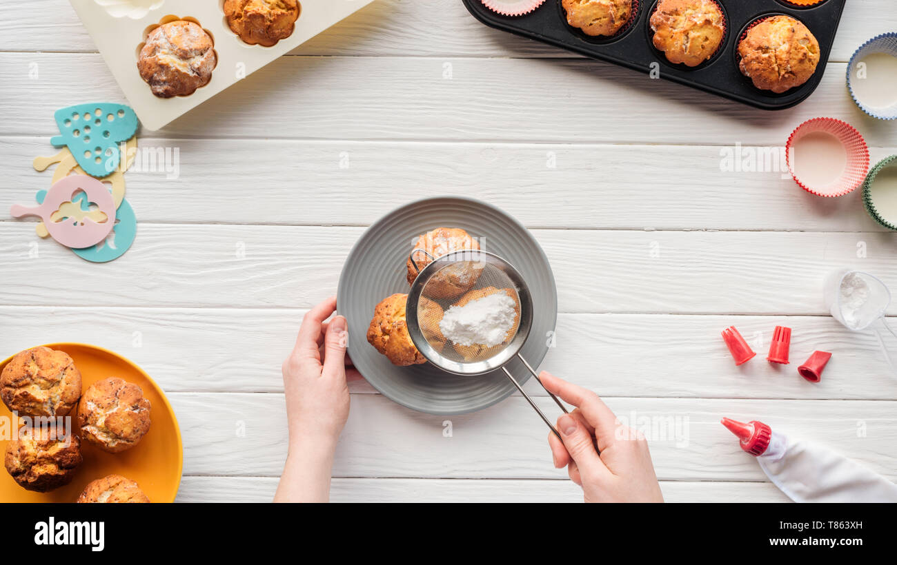 partial view of woman decorating cupcakes with powdered sugar on table with baking tools Stock Photo