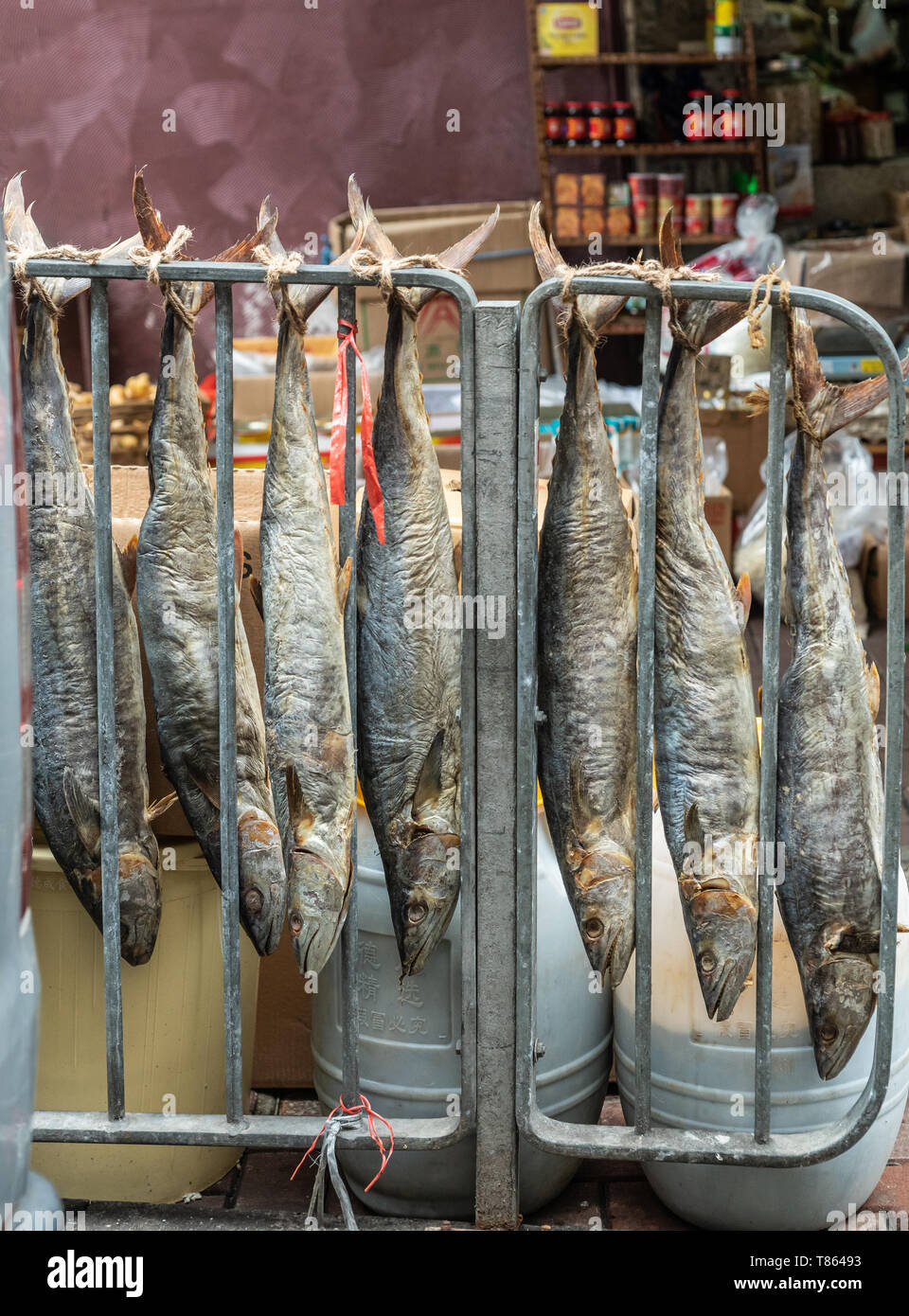 Hong Kong, China - March 8, 2019: Tai Po Market in New Territory. Several long dried fishes hang head down on metal grid in front of shop. Brown and s Stock Photo