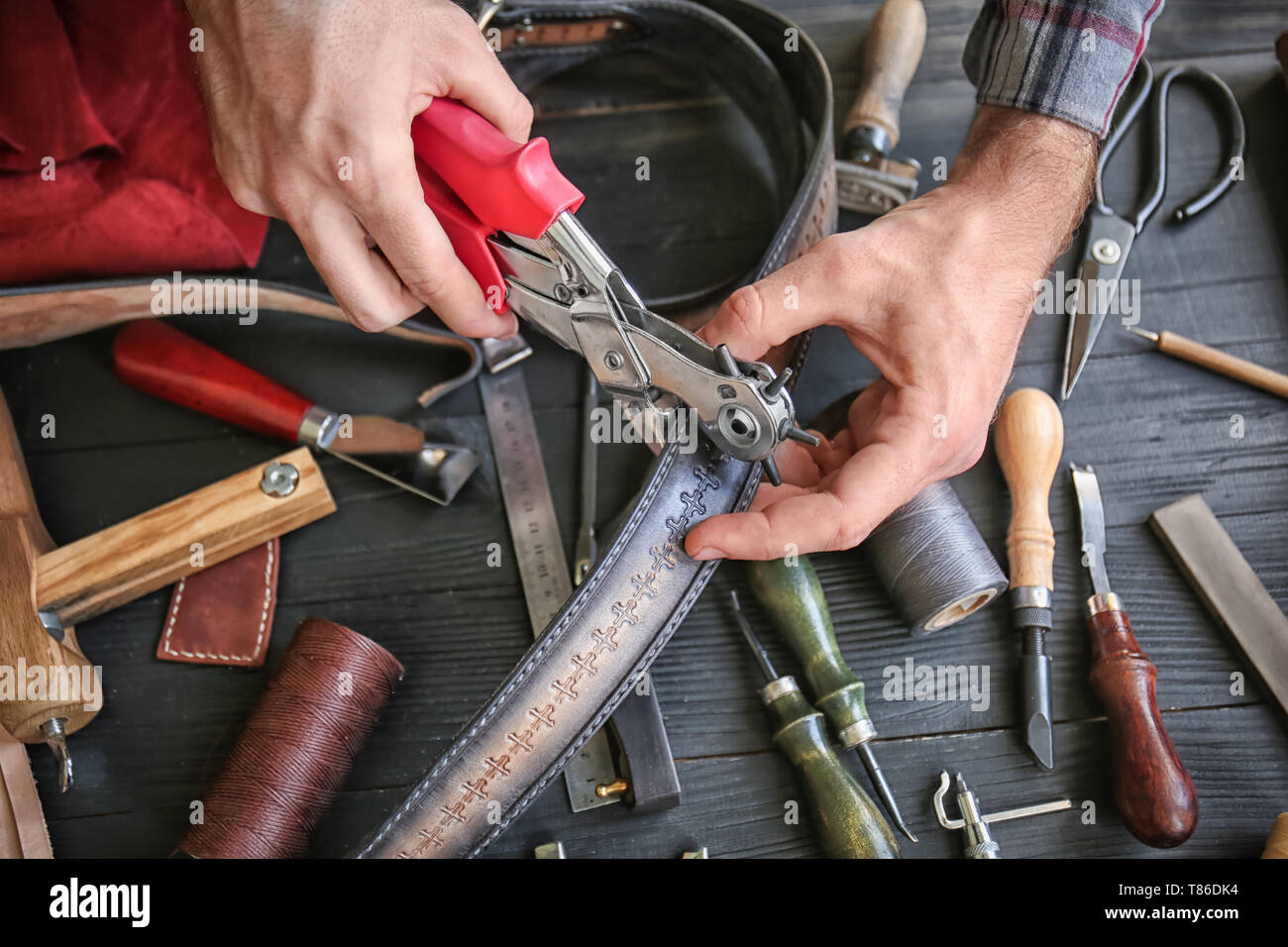 Man using leather punch while working with belt at factory, closeup Stock Photo