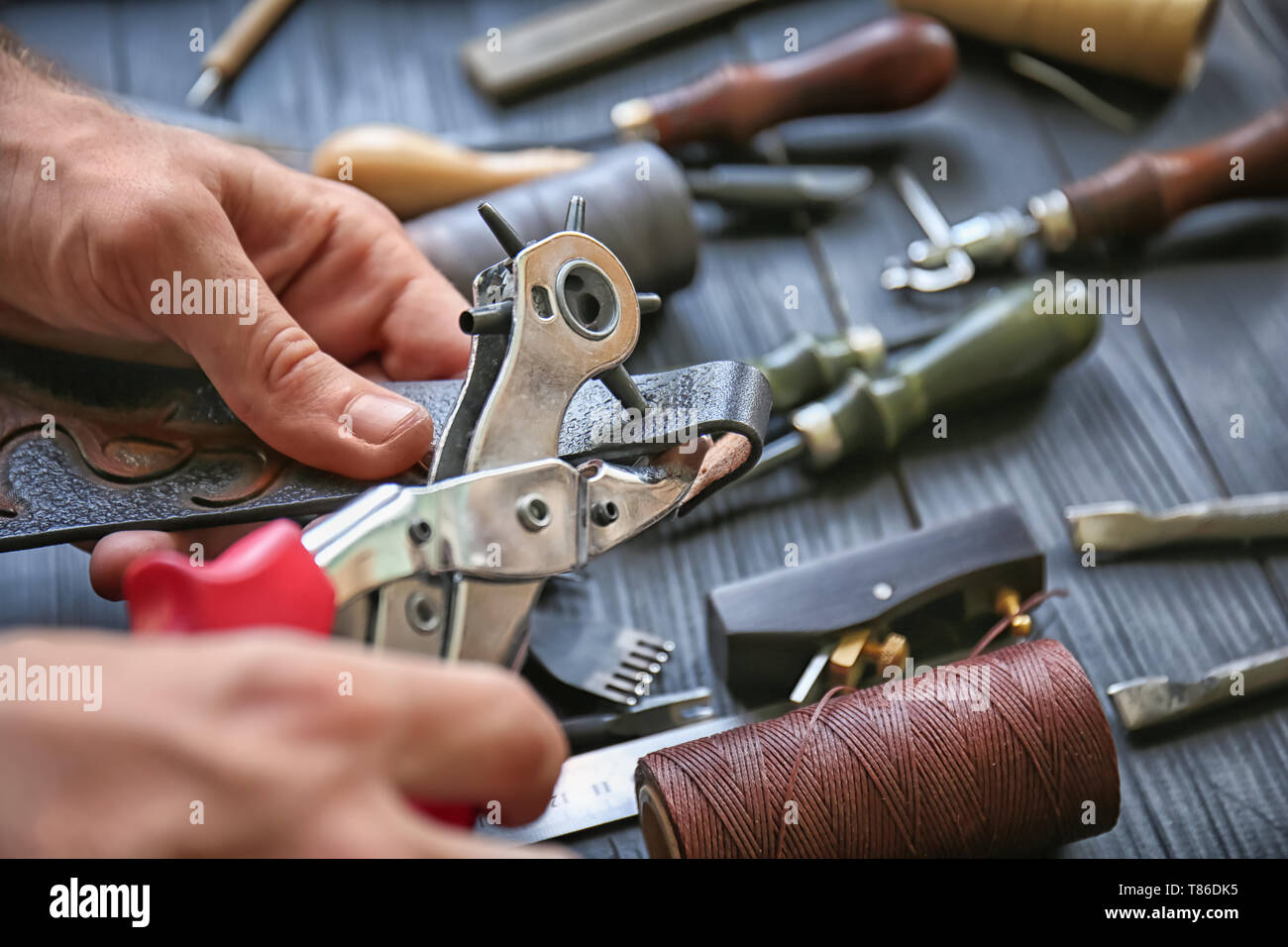 Man using leather punch while working with belt at factory, closeup Stock Photo