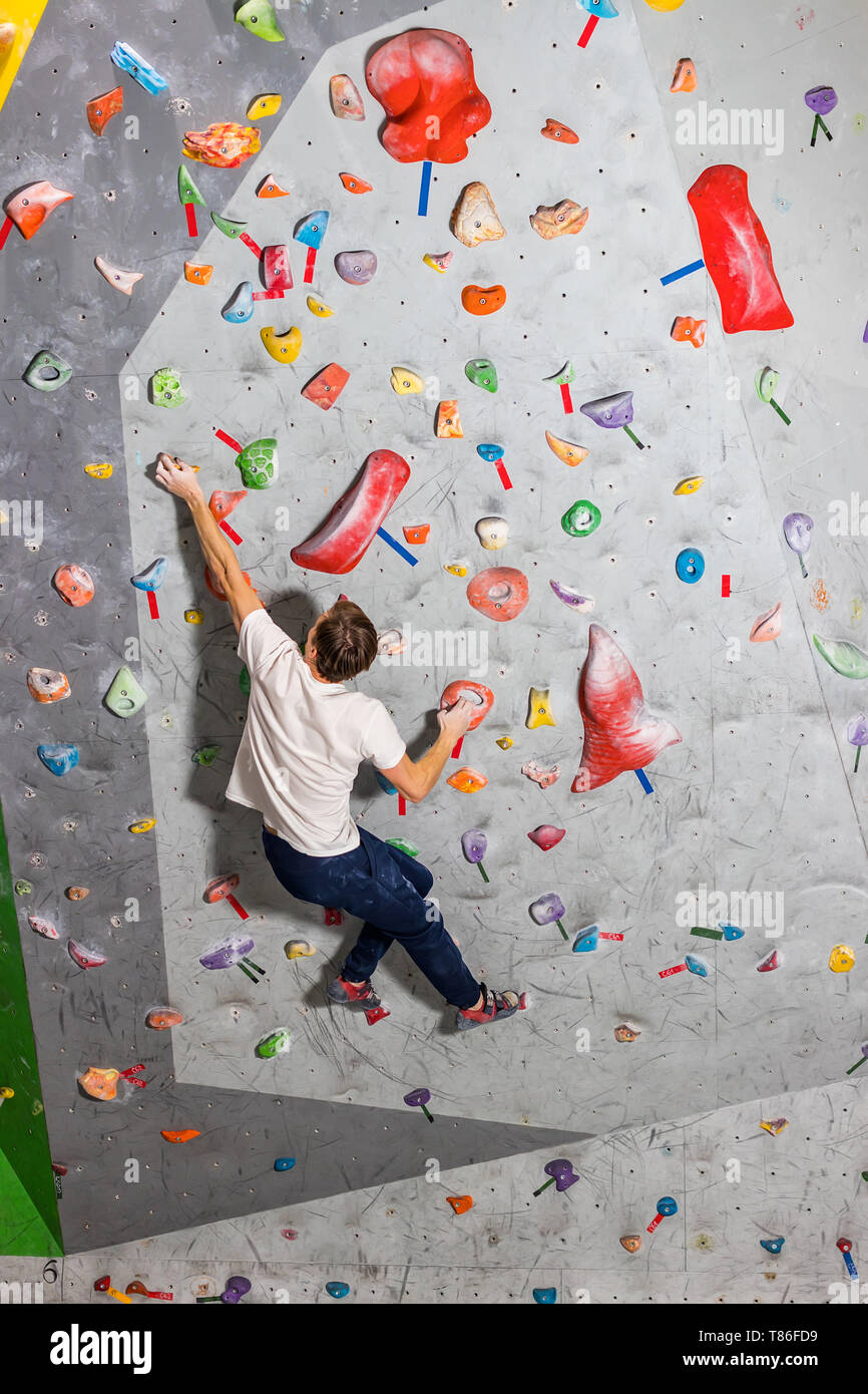 Rock climber man hanging on a bouldering climbing wall, inside on
