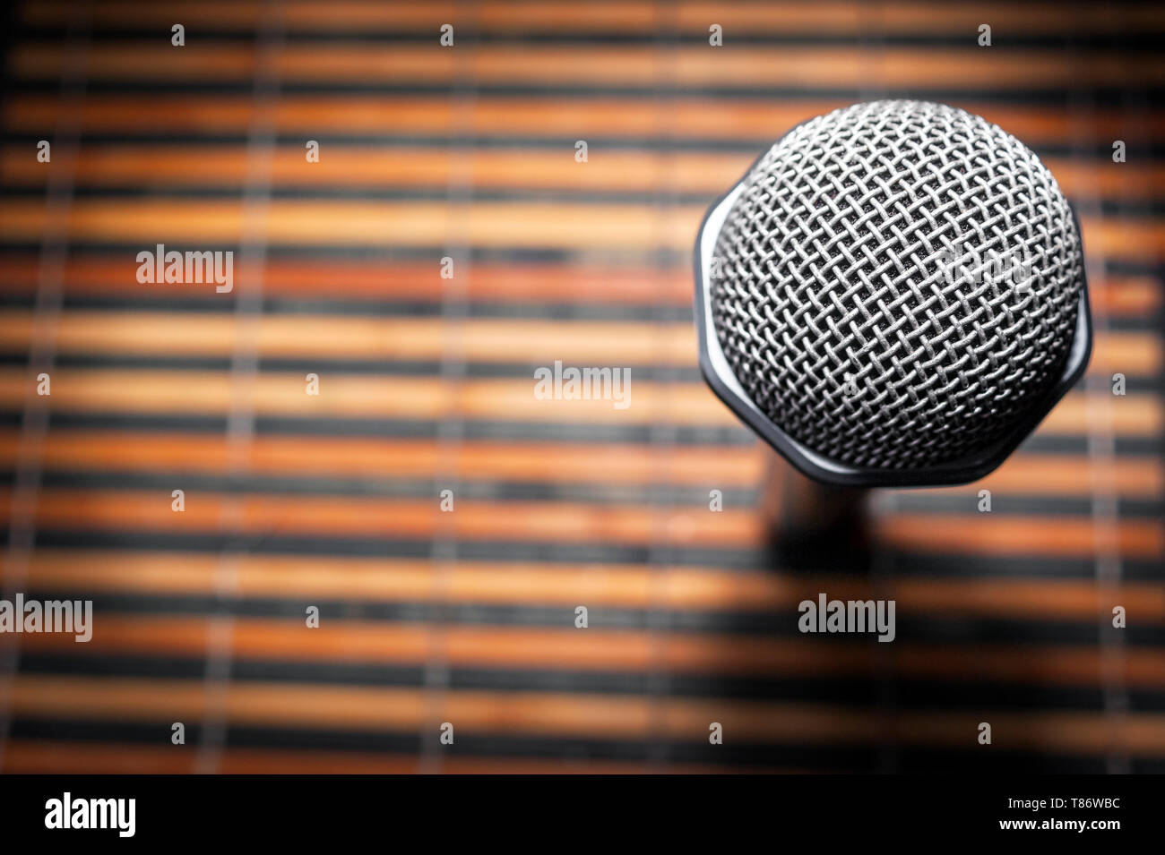 Top-Down View of A Microphone Head and Silver Grille on A Striped Yellow and Black Bamboo Mat Background. Karaoke Bar, Party Concept. Copy Space. Stock Photo
