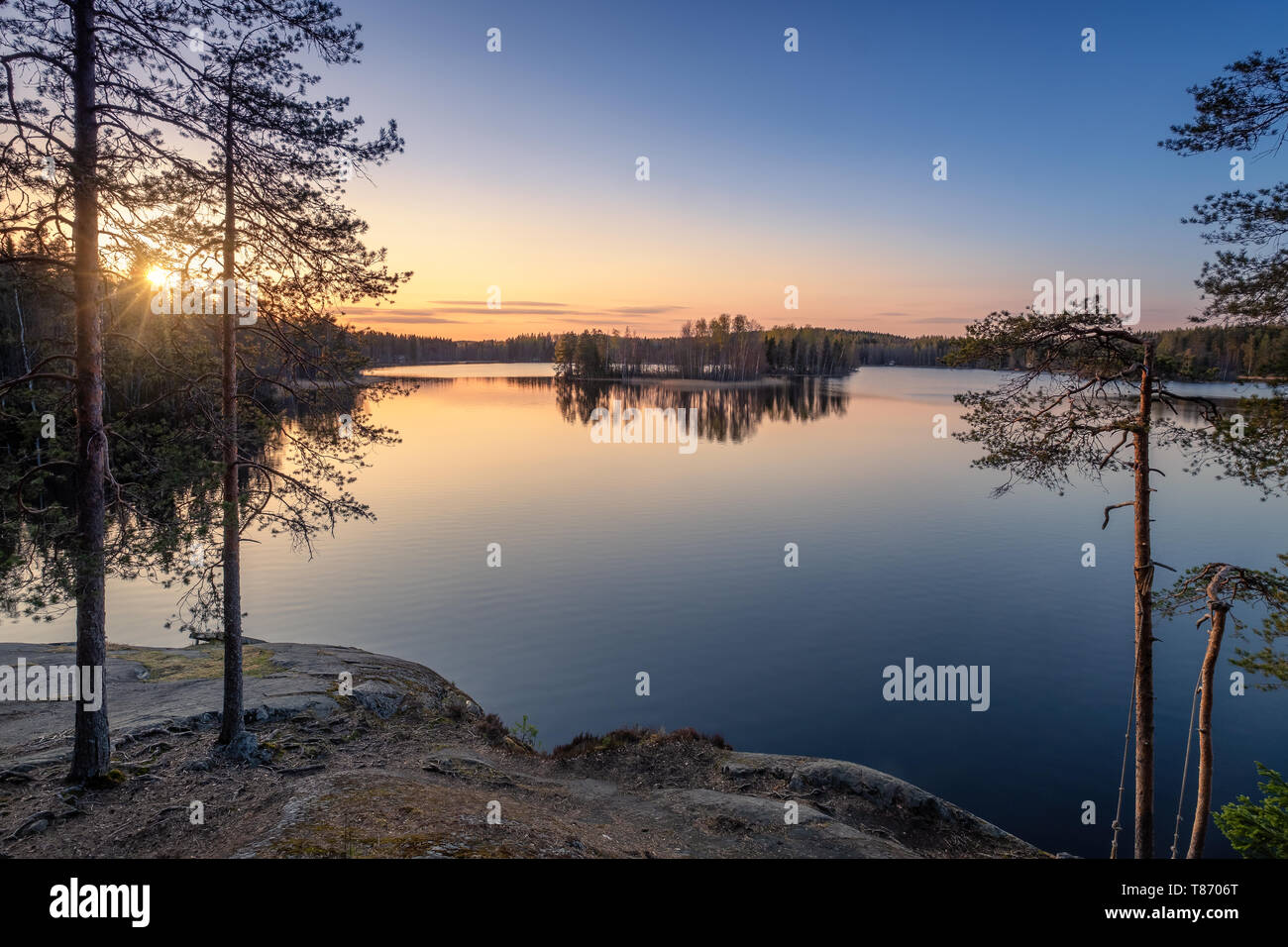 Scenic landscape with sunset, peaceful lake and tree roots at calm spring evening in Finland Stock Photo