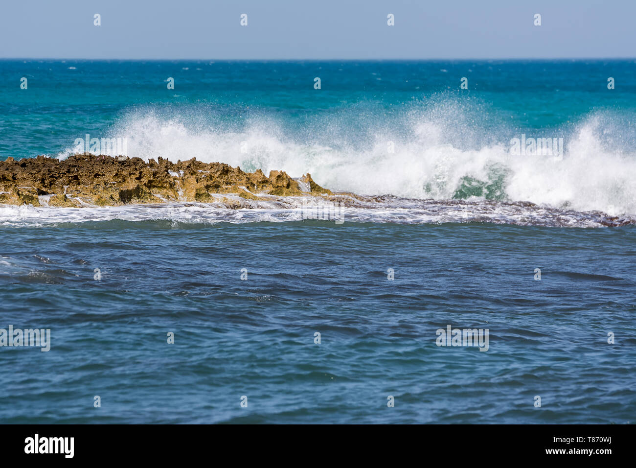 Onde spumeggianti che si infrangono sulla costa rocciosa e il mare blu Stock Photo