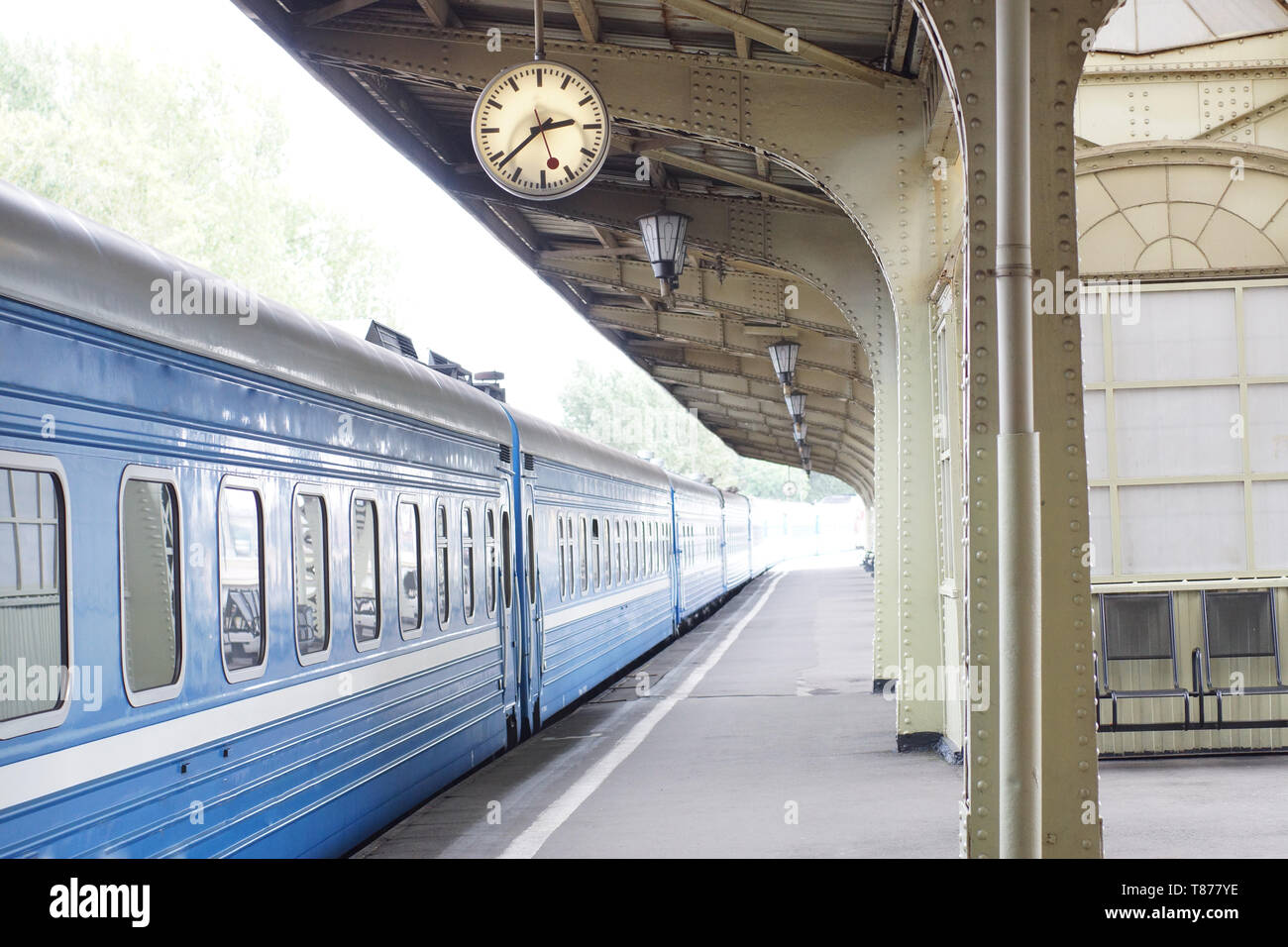 Blue train stands on the platform at the train station with a clock Stock Photo