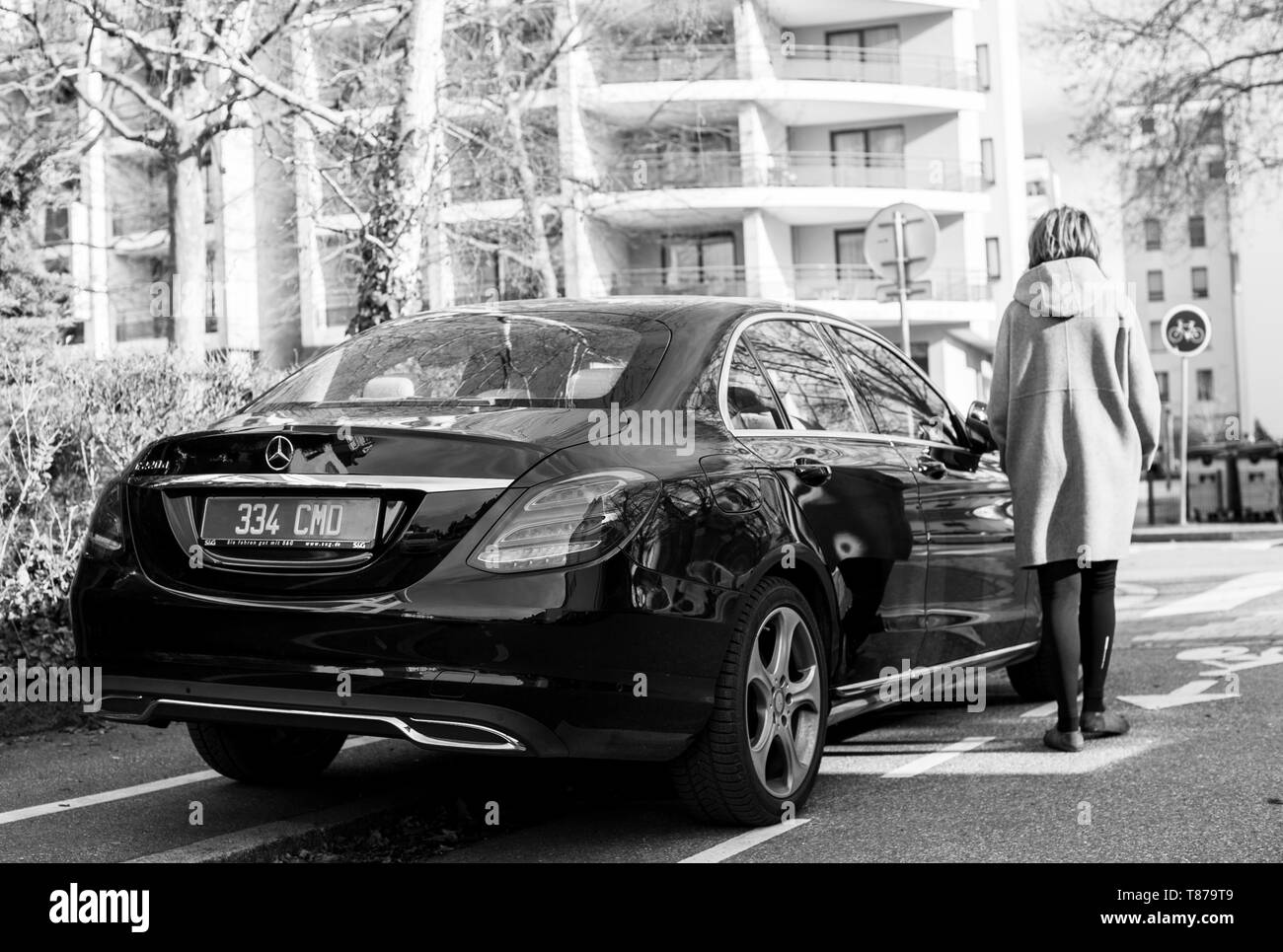 Strasbourg, France - Feb 23, 2017: Woman walking toward luxury Mercedes-Benz E220d diesel car parked on a calm street in French city black and white Stock Photo