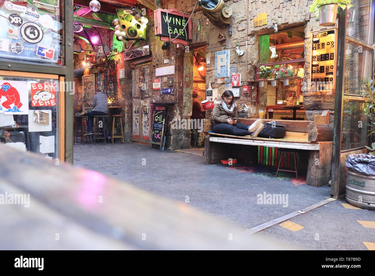 BUDAPEST, HUNGARY - april 2019: Interior view of the famous Szimpla Garden ruin pub with woman sitting on bench playing with mobile phone. Stock Photo