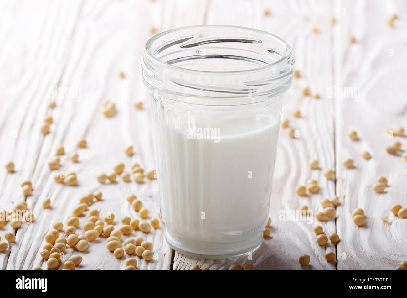 Non-dairy alternative Soy milk or yogurt in mason jar on white wooden table with soybeans aside Stock Photo