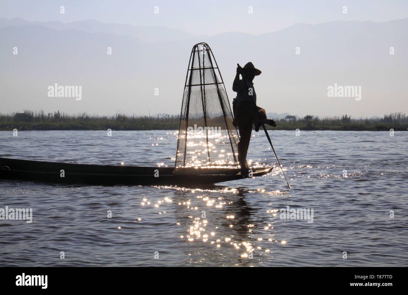 Silhouette of traditional fisherman balancing on his boat and rowing ...