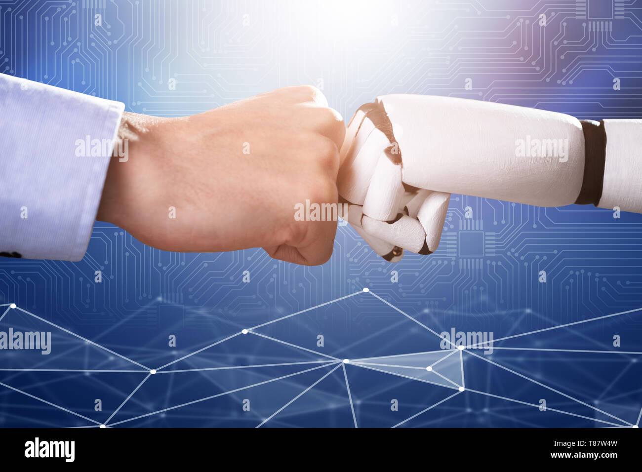 Robot And Human Hand Making Fist Bump On Blue Digital Backdrop Stock Photo