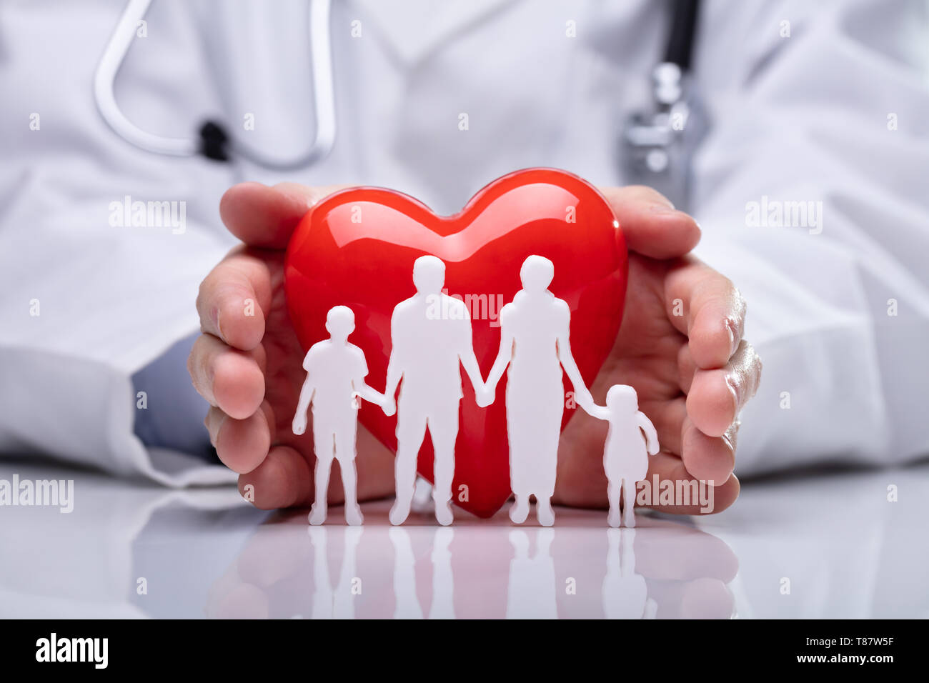 Close-up Of A Doctor's Hand Protecting White Family Paper Cut Out With Heart Shape Stock Photo