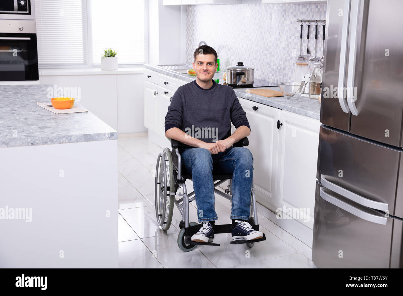Smiling Young Handicapped Man Sitting On Wheelchair In Kitchen Stock Photo