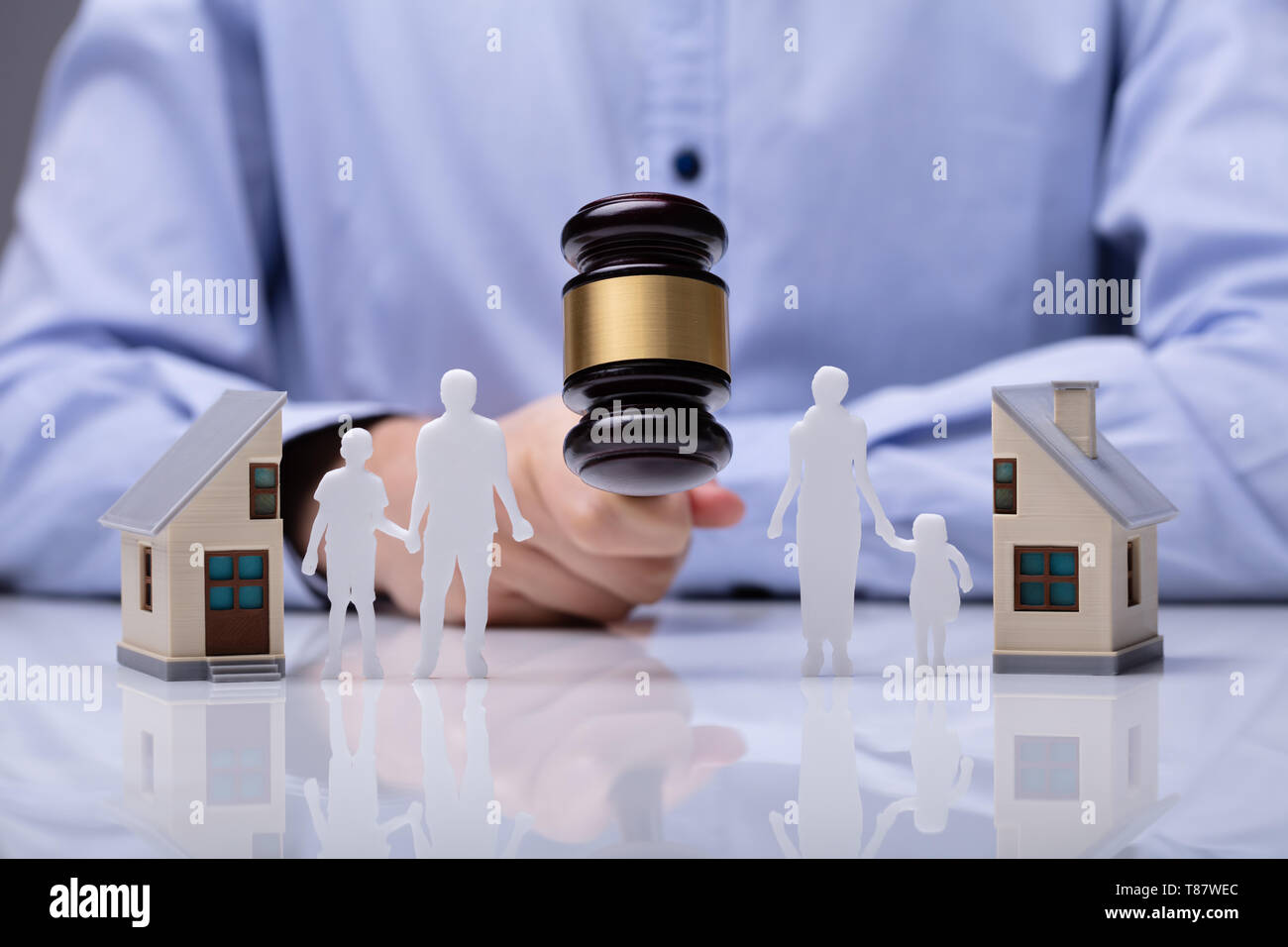 Close-up Of Mallet Showing Separation Of Family And House On Reflective Desk Stock Photo