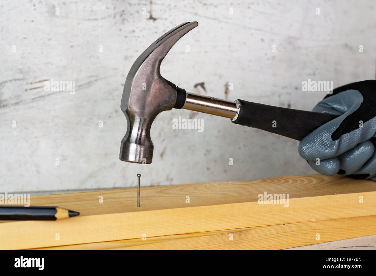 Male hand in a black construction glove hammering a nail with a hammer  against the background of a concrete wall Stock Photo - Alamy