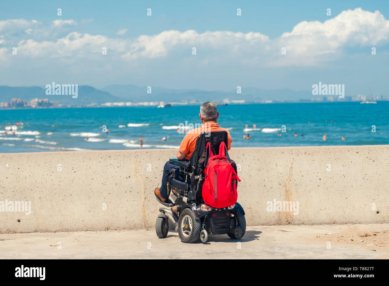 Lonely man on electric wheelchair looking at the beach. Disabled person