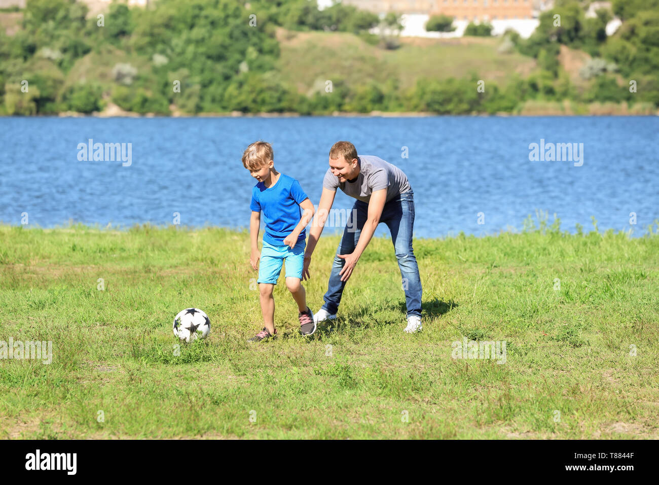 Happy father and son playing football near river Stock Photo Alamy