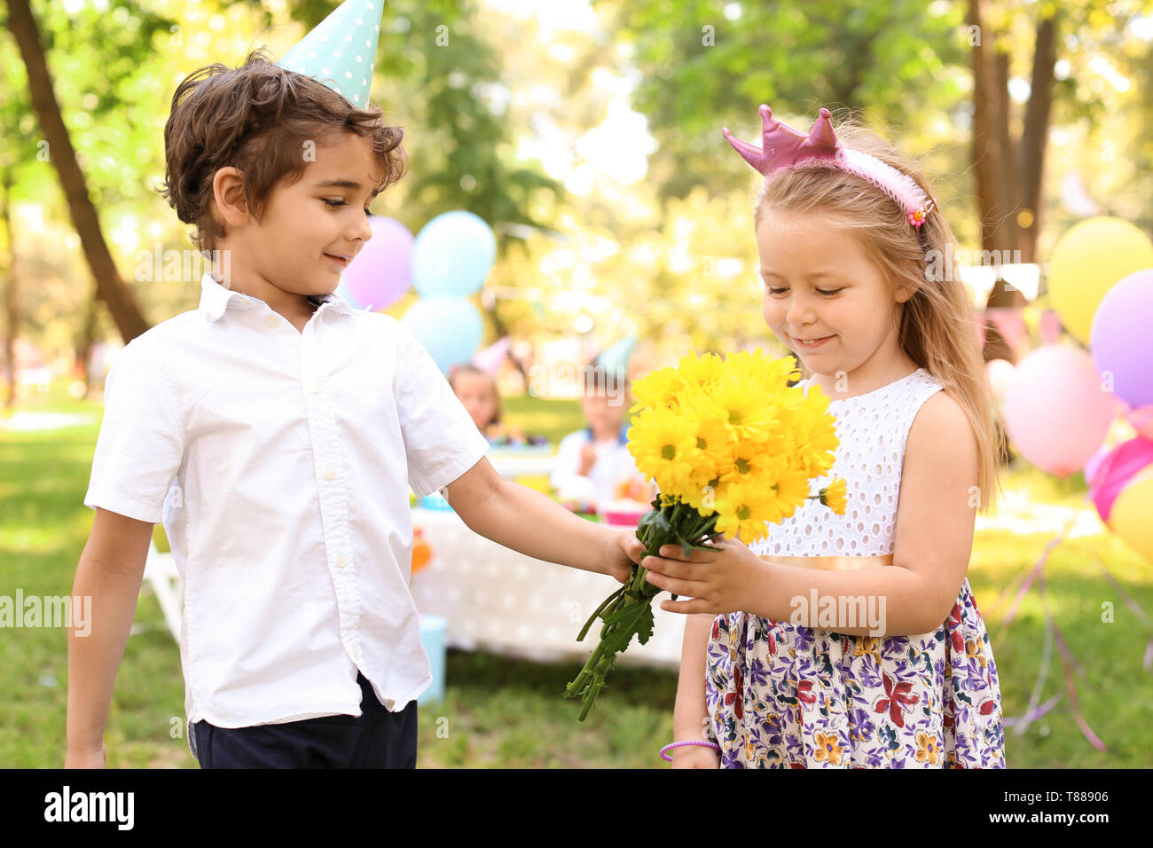 Little girl receiving flowers from cute boy at birthday party outdoors